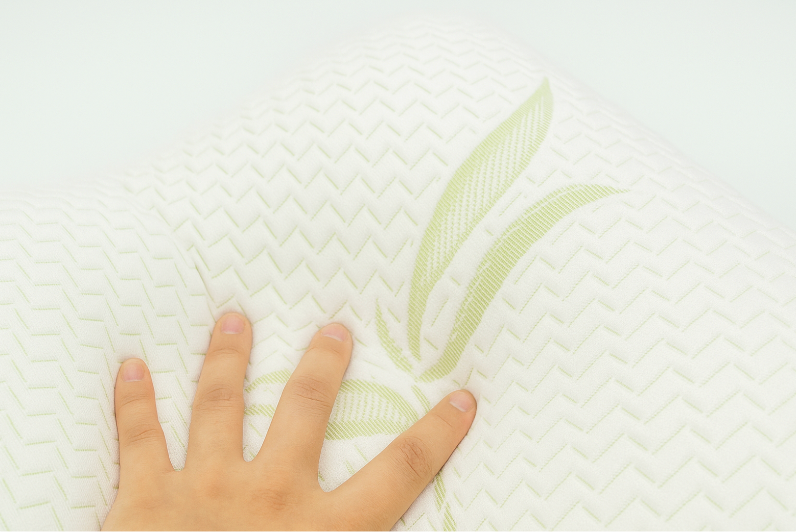 Close-up hand pressing on a bamboo memory foam pillow with soft white cover and green bamboo leaf design, showing contour support and comfort.