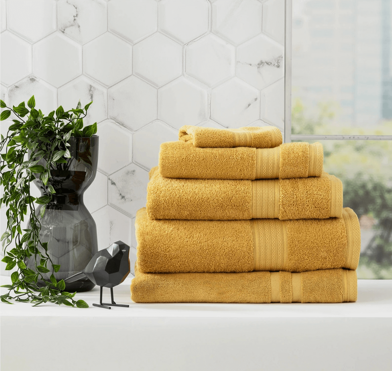 Stack of Adorearth™ organic bamboo towels in yellow on a bathroom counter with a plant and decorative black bird.