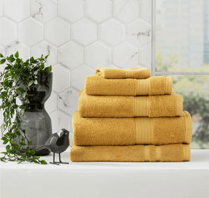 Stack of Adorearth™ organic bamboo towels in yellow on a bathroom counter with a plant and decorative black bird.
