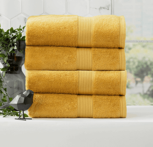 Four folded golden yellow Adorearth™ Organic Bamboo Towels stacked beside a decorative plant and black bird figurine.